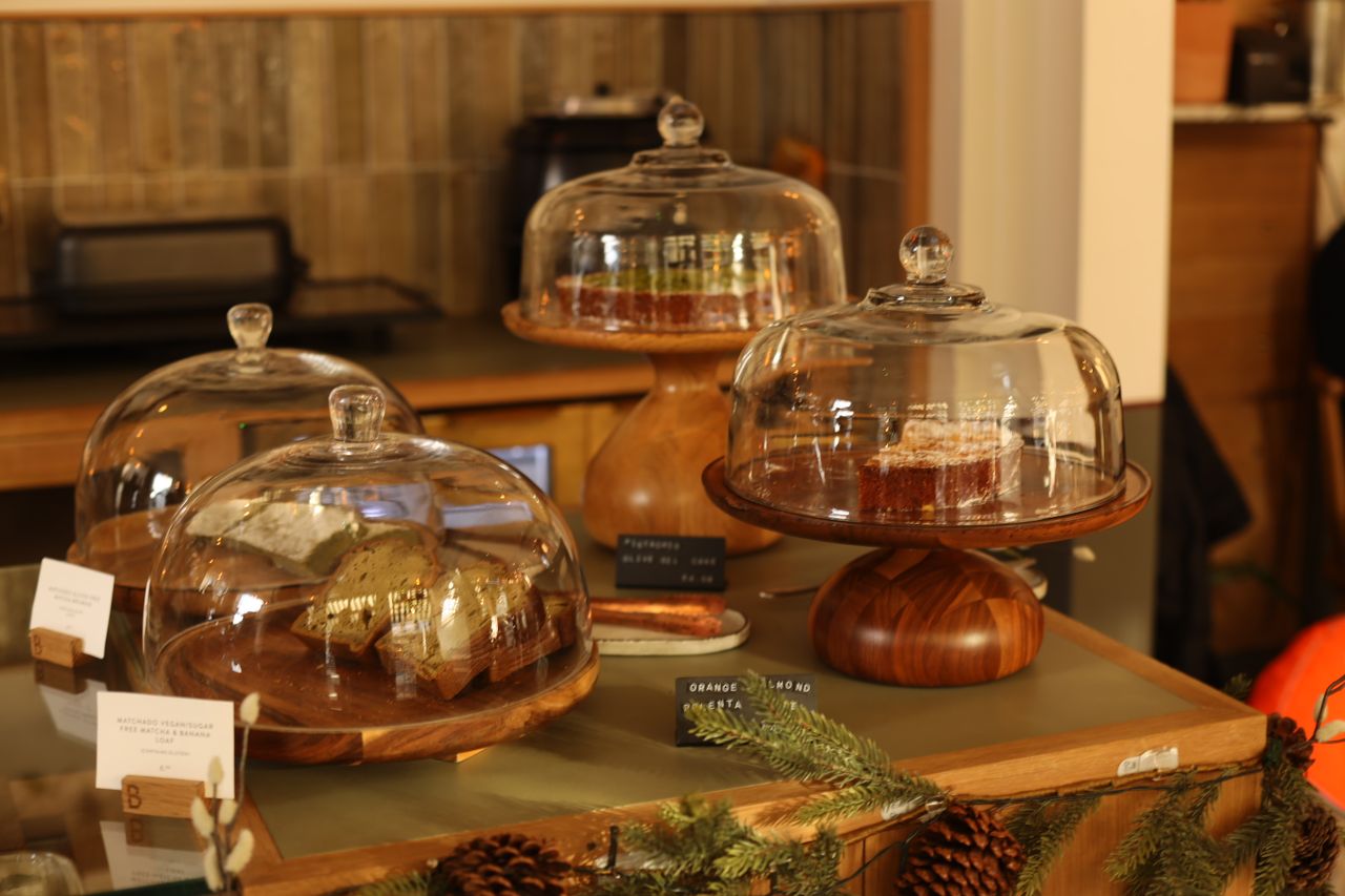 about-img Showcase of pastries and cakes under glass domes on wooden stands in a bakery setting.
