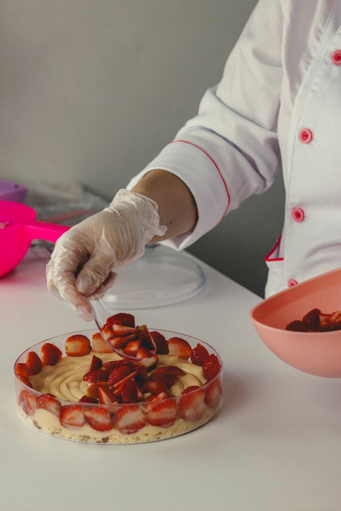 contact-img Chef skillfully decorates a strawberry cake in a professional kitchen setting, showcasing culinary art.