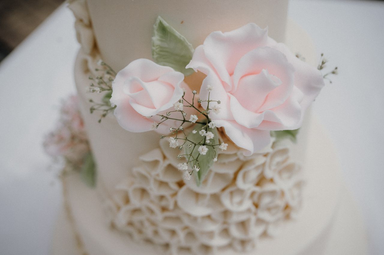 services-01 Close-up of an elegant wedding cake adorned with delicate pink sugar roses.
