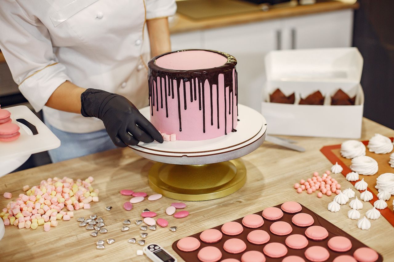 Mastering the First Impression: Your intriguing post title goes here From above crop female cook in uniform and latex gloves placing small sweets on bottom of cake placed on stand near desserts in confectionery